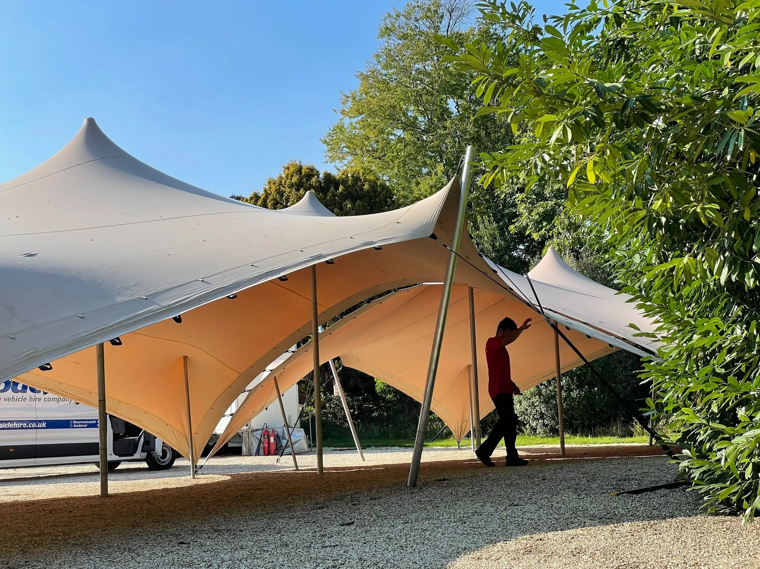 Sand-coloured stretch tent rigged on gravel with crew setting up