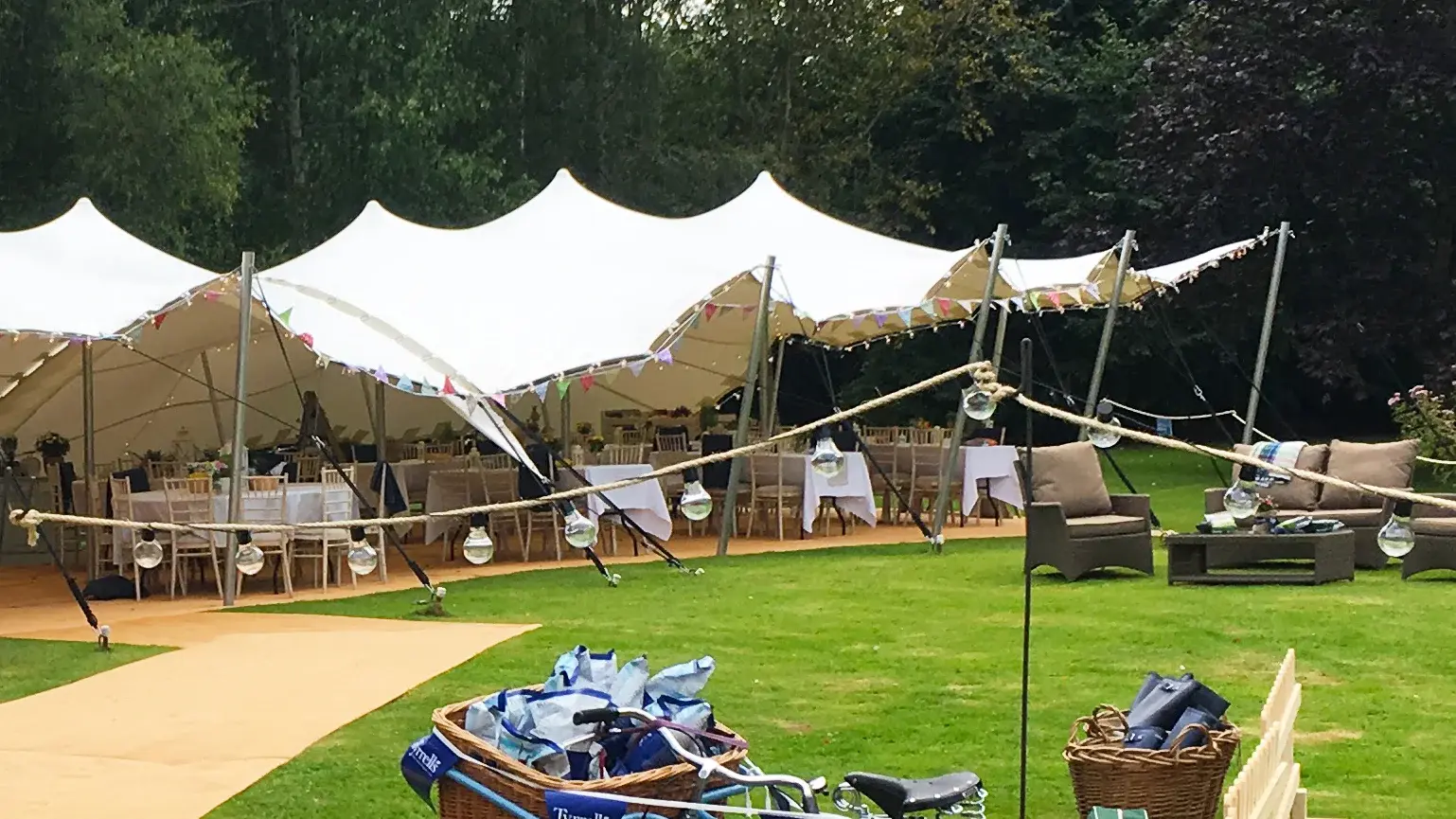 White stretch tents with bunting and festoon lights over a garden lawn party
